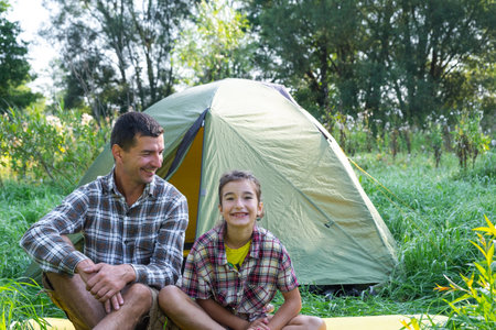 Portrait of a happy family dad and daughter sitting in the morning near the outdoor camping tent, camping, family hiking tripの写真素材