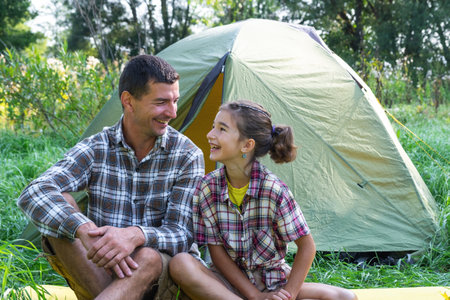 Portrait of a happy family dad and daughter sitting in the morning near the outdoor camping tent, camping, family hiking tripの写真素材