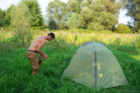 The man installs and assembles tourist tent in a camping in nature in the forest. Domestic tourism, active summer holidays, family adventures. Ecotourism, sport, hikeの写真素材