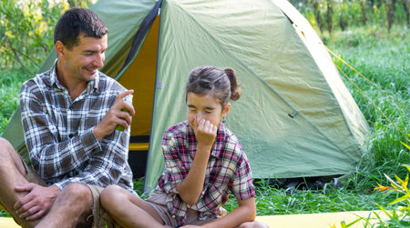 Dad sprays repellent on daughter outdoor camping and picnicking near a tentの写真素材