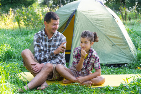 Dad sprays repellent on daughter outdoor camping and picnicking near a tentの写真素材