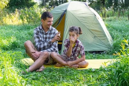 Dad sprays repellent on daughter outdoor camping and picnicking near a tentの写真素材