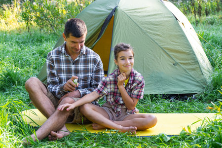 Dad sprays repellent on daughter outdoor camping and picnicking near a tentの写真素材