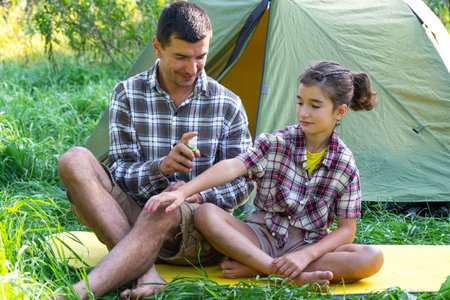 Dad sprays repellent on daughter outdoor camping and picnicking near a tentの写真素材