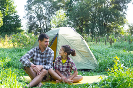 Portrait of a happy family dad and daughter sitting in the morning near the outdoor camping tent, camping, family hiking tripの写真素材