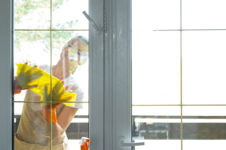 Woman in rubber gloves and apron manually washes window balcony of house with rag cleaner and mop...
