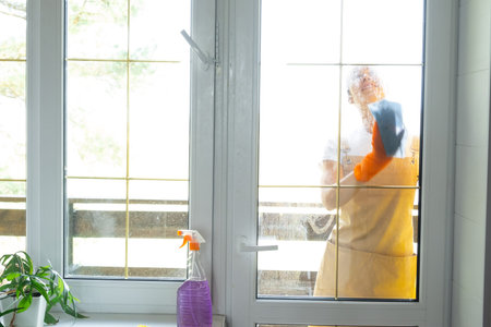 Woman in rubber gloves and apron manually washes window balcony of house with rag cleaner and mop...