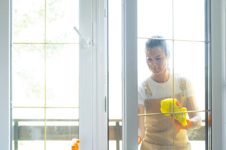 Woman in rubber gloves and apron manually washes window balcony of house with rag cleaner and mop...