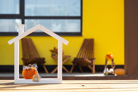 Autumn decor on porch of yellow house outside of pumpkin, lantern, garlands and figure of tiny home and key. Halloween party, autumn mood, Harvest festivalの写真素材