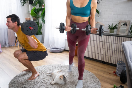 Woman and man in a sports uniform is engaged in fitness and strength training with a barbell and dumbbells at home in the interior and catの写真素材