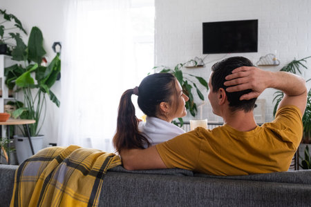 Man and woman at home in a white interior sits on the couch and watches TV, black screen mock up. Home recreation, leisure, love, family, dateの写真素材