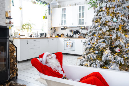 Santa is lying resting in New bathtub under festive Christmas tree as New Year's gift in interior of white modern decorated kitchen. Interior renovation and design, construction and home improvementの写真素材