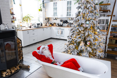 Santa is lying resting in New bathtub under festive Christmas tree as New Year's gift in interior of white modern decorated kitchen. Interior renovation and design, construction and home improvementの写真素材