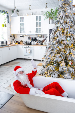 Santa is lying resting in New bathtub under festive Christmas tree as New Year's gift in interior of white modern decorated kitchen. Interior renovation and design, construction and home improvementの写真素材