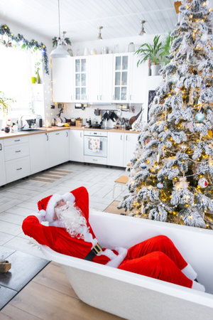 Santa is lying resting in New bathtub under festive Christmas tree as New Year's gift in interior of white modern decorated kitchen. Interior renovation and design, construction and home improvementの写真素材