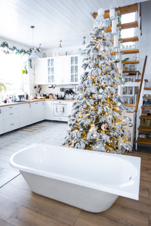 New bathtub under festive Christmas tree as New Year's gift in interior of white modern decorated kitchen. Interior renovation and design, construction and home improvementの写真素材