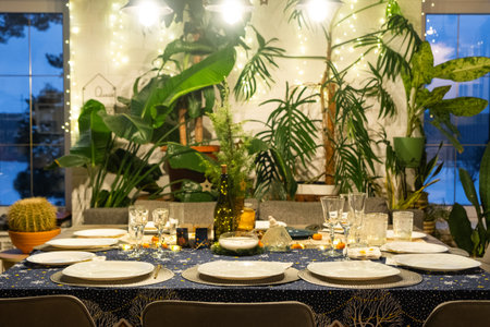 A festive table set for guests for Christmas and New Year, in the living room, plates, bottles, glasses, potted plants, fairy lightsの写真素材