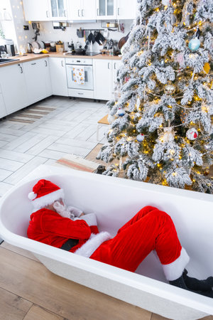 Santa is lying resting in bathtub under festive Christmas tree as New Year's gift in interior of white modern decorated kitchen. Interior renovation and design, construction and home improvementの写真素材