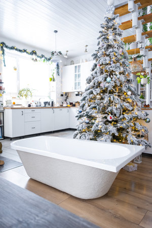 New bathtub under festive Christmas tree as New Year's gift in interior of white modern decorated kitchen. Interior renovation and design, construction and home improvementの写真素材