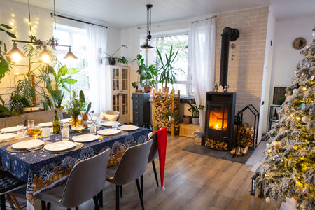 Festive interior of house is decorated for Christmas and New Year in loft style with black stove, fireplace, Christmas tree. Warm studio room with set table, burning wood, cozy and heating of homeの写真素材