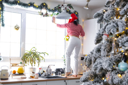A woman in a Santa hat cleans a kitchen window with Christmas decorations, preparing for the New Year, decorating and tidying up the houseの写真素材