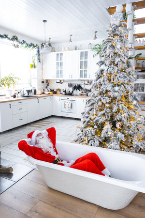 Santa is lying resting in New bathtub under festive Christmas tree as New Year's gift in interior of white modern decorated kitchen. Interior renovation and design, construction and home improvementの写真素材