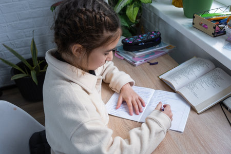 A schoolgirl girl prepares homework for school at the tableの写真素材