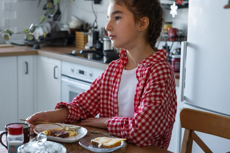 The girl has breakfast in the kitchen with scrambled eggs and a sandwich at the table in the morning