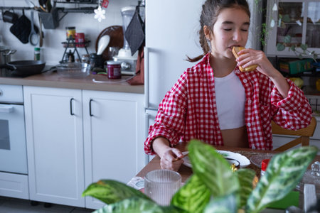 The girl has breakfast in the kitchen with scrambled eggs and a sandwich at the table in the morning