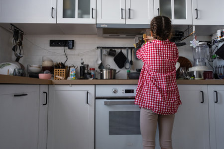 The girl cooks her own breakfast in the kitchen, fried eggs in a frying panの写真素材
