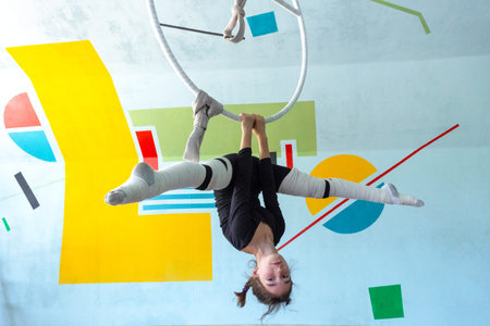 Young girl in black sportswear practicing aerial hoop movements, acrobatic technique, safety,...