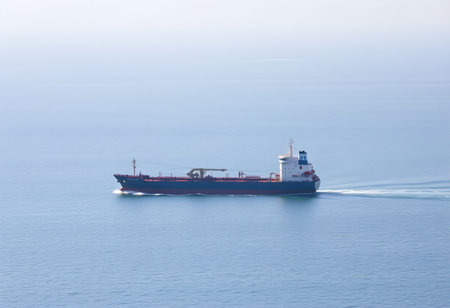 Large red cargo ship in the open sea with blue sky background.の素材