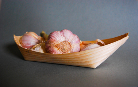 Pink garlic heads in a natural wooden container with gray backgroundの写真素材