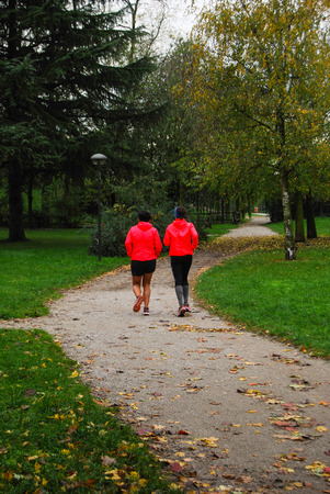 Two girls running on a dirt and little road with orange jacketの写真素材