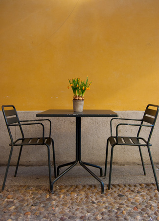 Two chairs and a table with daffosils on it outside an Italian restaurant - center of Milanの写真素材