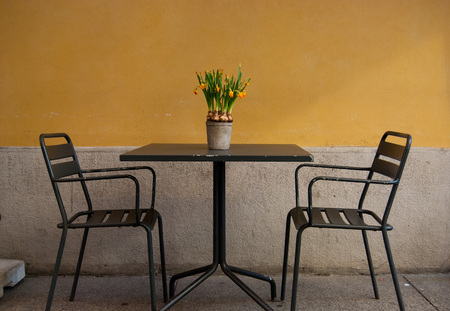 Two chairs and a table with daffosils on it outside an Italian restaurant - center of Milanの写真素材