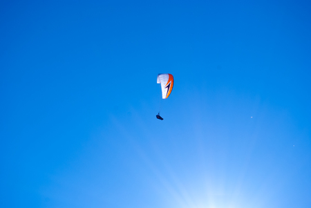 Descent of a paraglider in the blue sky and in the rays of the sunの写真素材