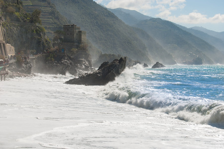 Wave breaks on the rocky coast and beach of 5 Terre with castle and path next toの写真素材