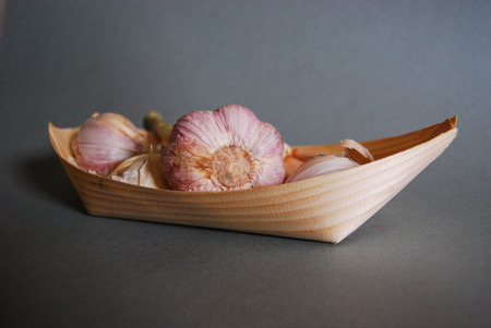 Pink garlic heads in a natural wooden container with gray backgroundの写真素材