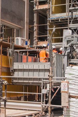 View of a building site with three workers with orange jacket and helmetの写真素材