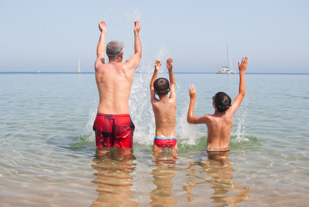 One adult and two children are creating splashes of joy in the seaの写真素材