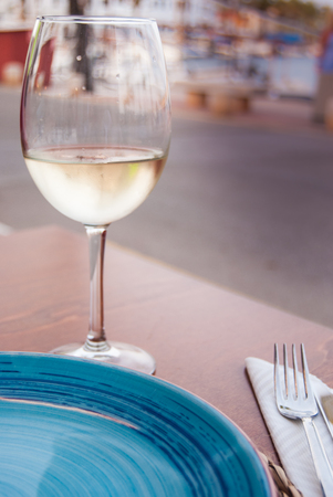 Flute of white wine with light blue ceramic dish on the table of a cafe restaurantの写真素材