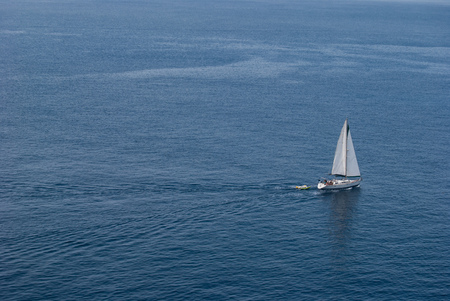 White sailboat with two lifeboats behind amidst the calm seaの写真素材