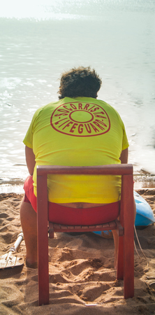 Man with yellow lifeguard t-shirt looking at the sea from the beachの写真素材
