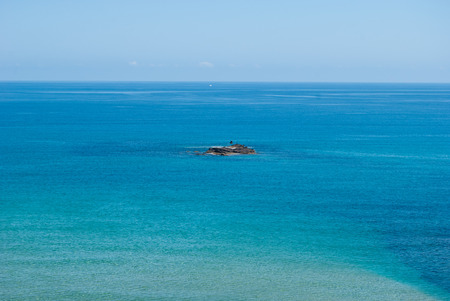 Rock rises from the crystalline and a bit rippled sea in a windy dayの写真素材