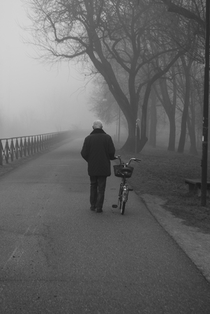 Man walking while he pulls his bike during a foggy dayの写真素材