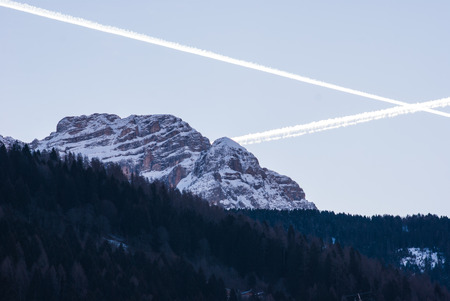 View of the Dolomites mountains with a cross of illuminated wakes left from two planeの写真素材