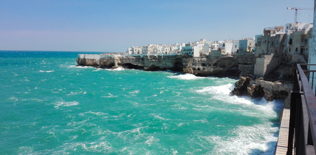 Waves crashing on the rocky cliff and white houses of Polignano a Mareの写真素材