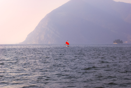 Lonely sailboat with red and white sail in a day with mistの写真素材