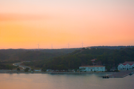 Four wind turbines during the sunset on Mahon harbor and reflection on the seaの写真素材